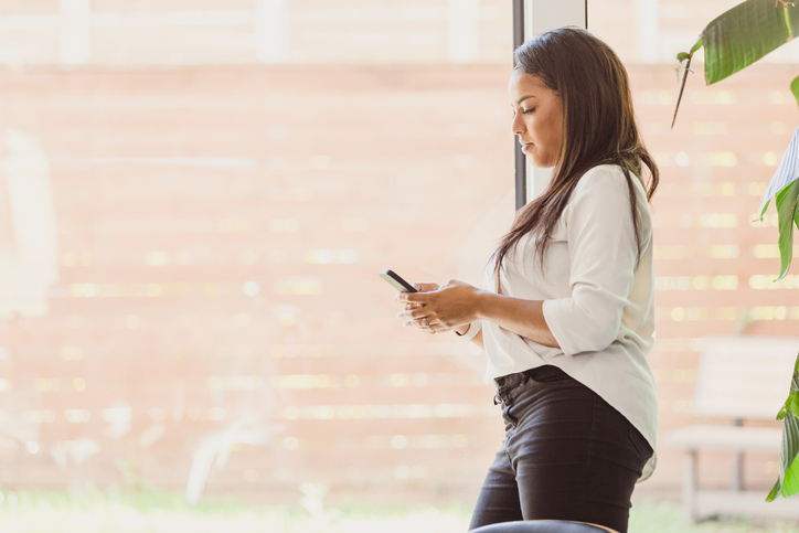 Mid adult woman stands by big window to text message