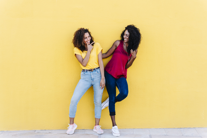 Girlfriends smiling while having fun against yellow wall