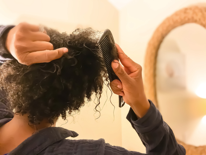 mid adult african-american woman detangles wet natural hair with comb