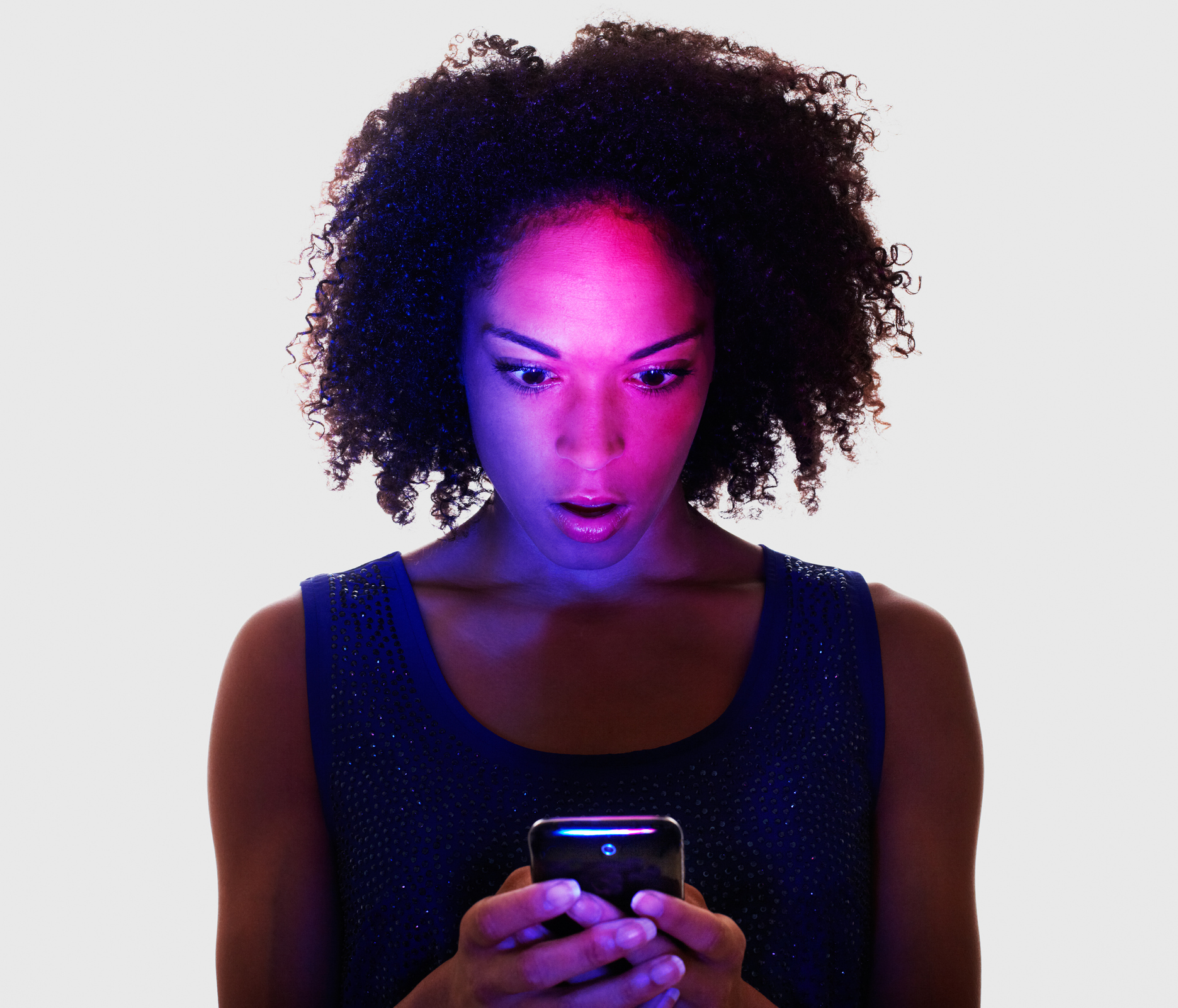 Woman lit by smart phone looking surprised.