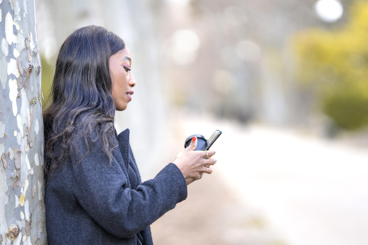 young pretty black woman resting drinking coffee and using smartphone