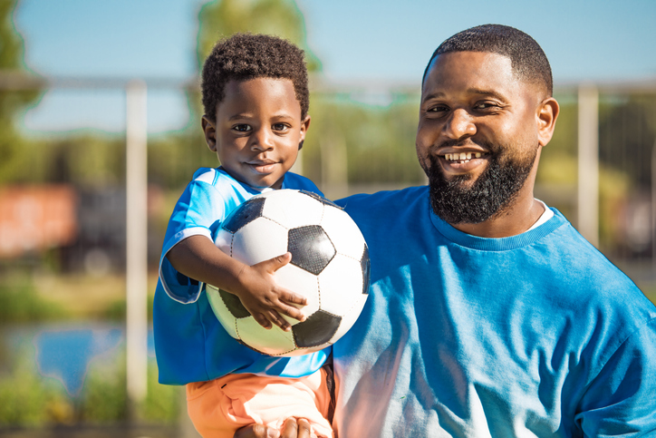 Black father and young son training on the football pitch