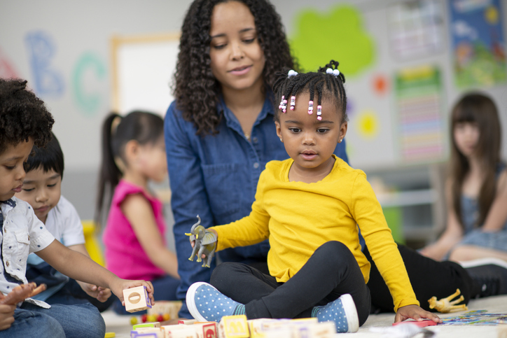 Kind female teacher instructing happy preschool students