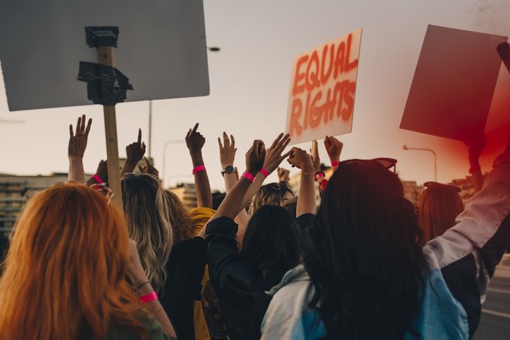 Rear view of young women protesting for equal rights while marching in city