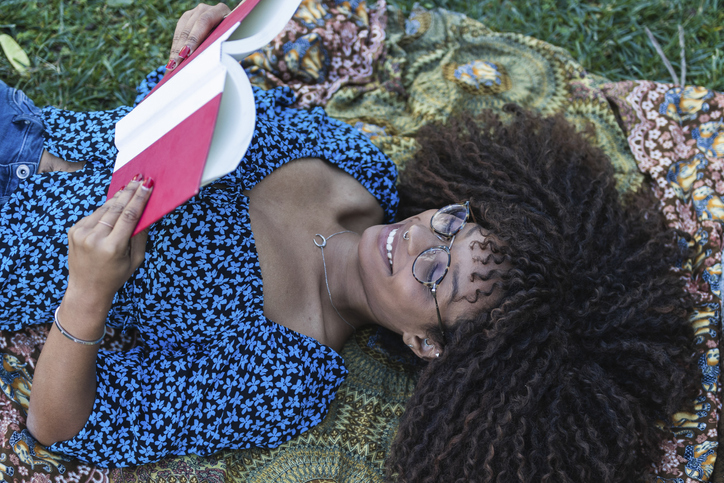 Happy young woman lying on blanket while reading book in public park