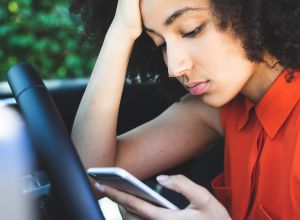 Woman waiting in the car and, annoyed, scrolling social media