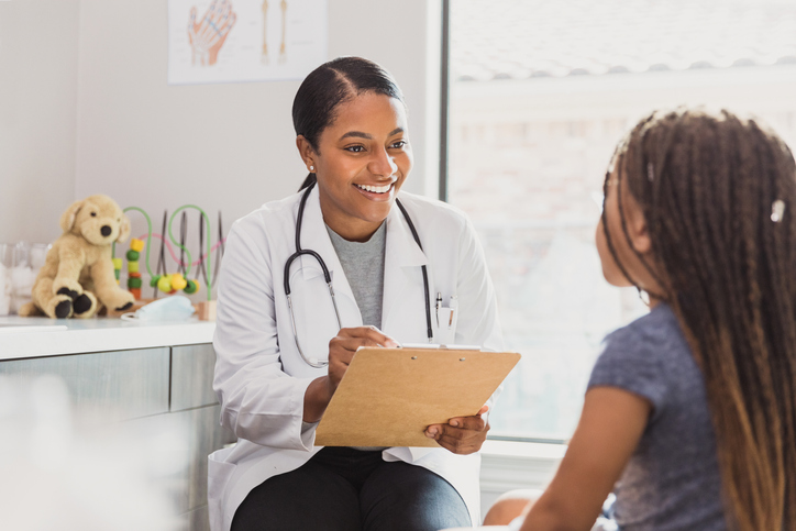Mid adult pediatrician smiles as she listens to girl