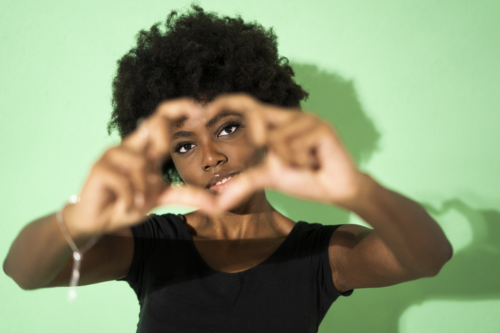 Woman making heart shape with finger while standing against green background