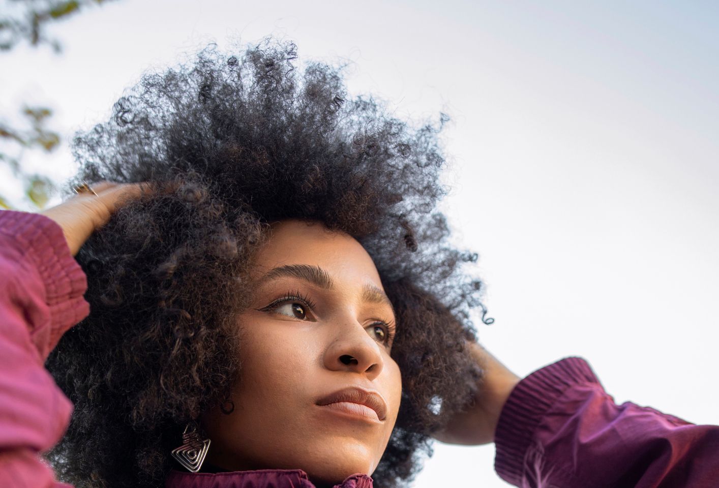 Afro young woman with hand in hair day dreaming against clear sky