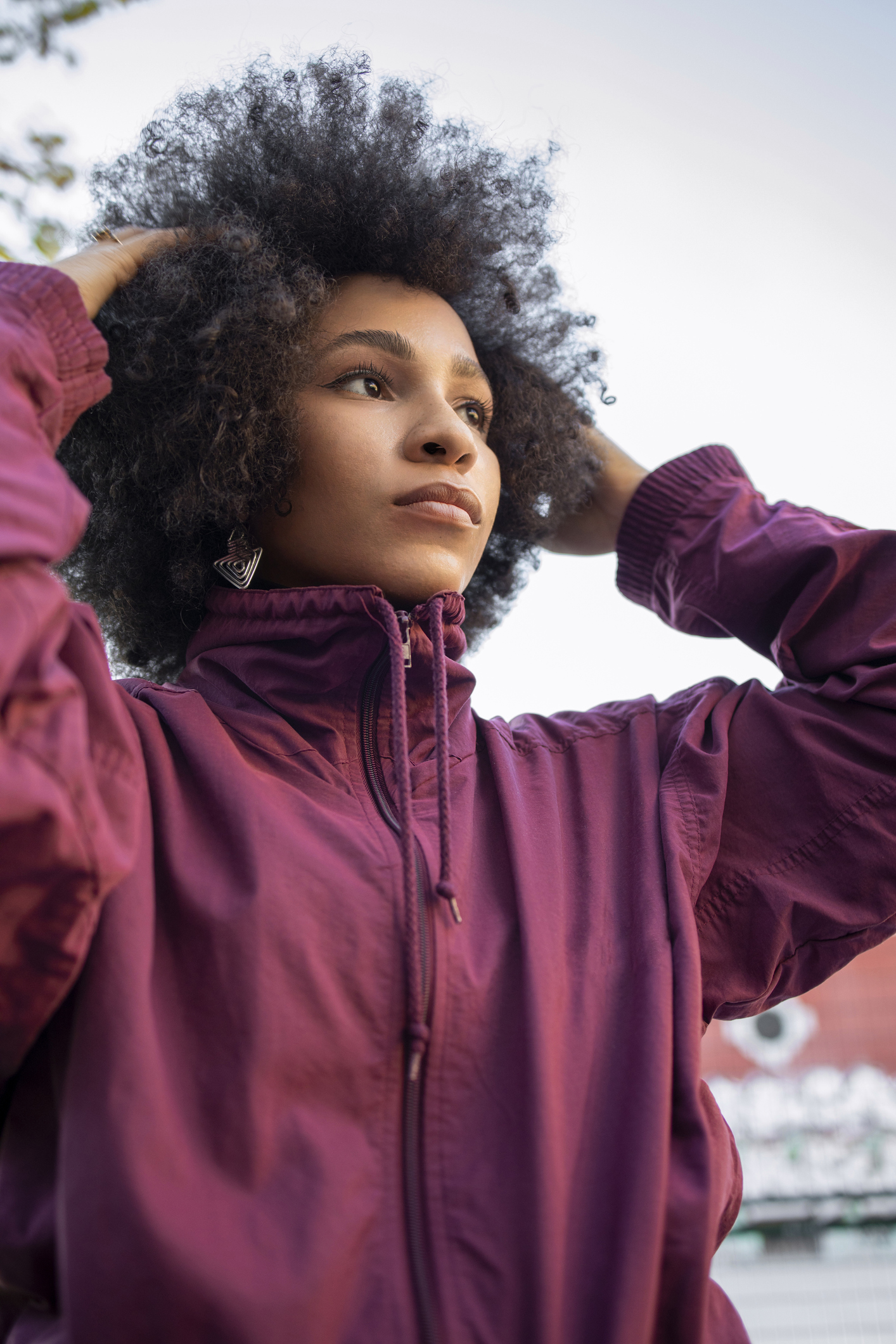 Afro young woman with hand in hair day dreaming against clear sky