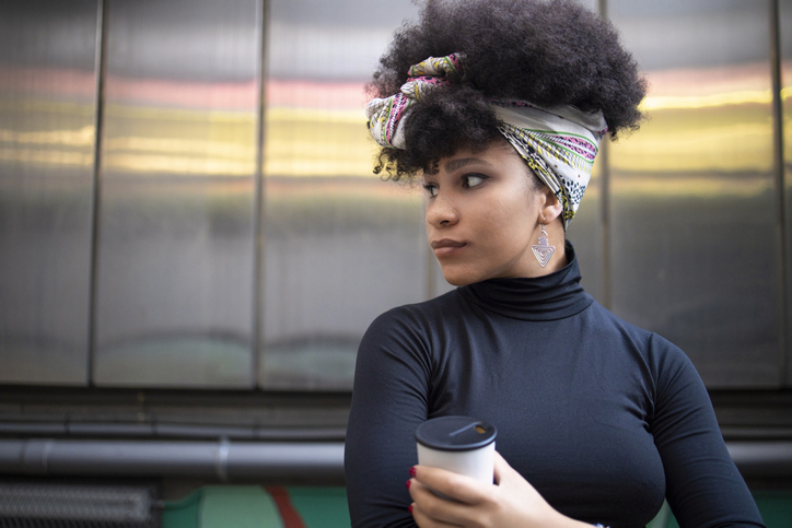 Afro young woman day dreaming while holding disposable coffee cup against wall