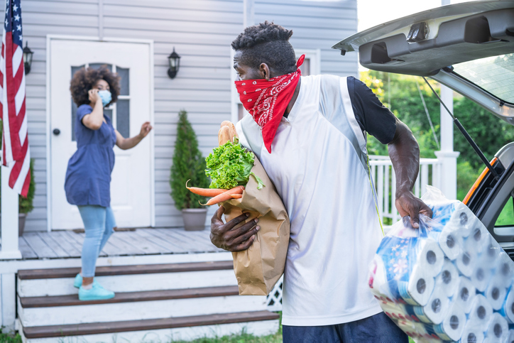 African ethnicity couple with protective face mask delivering food ordered online in front of the porch, during COVID-19