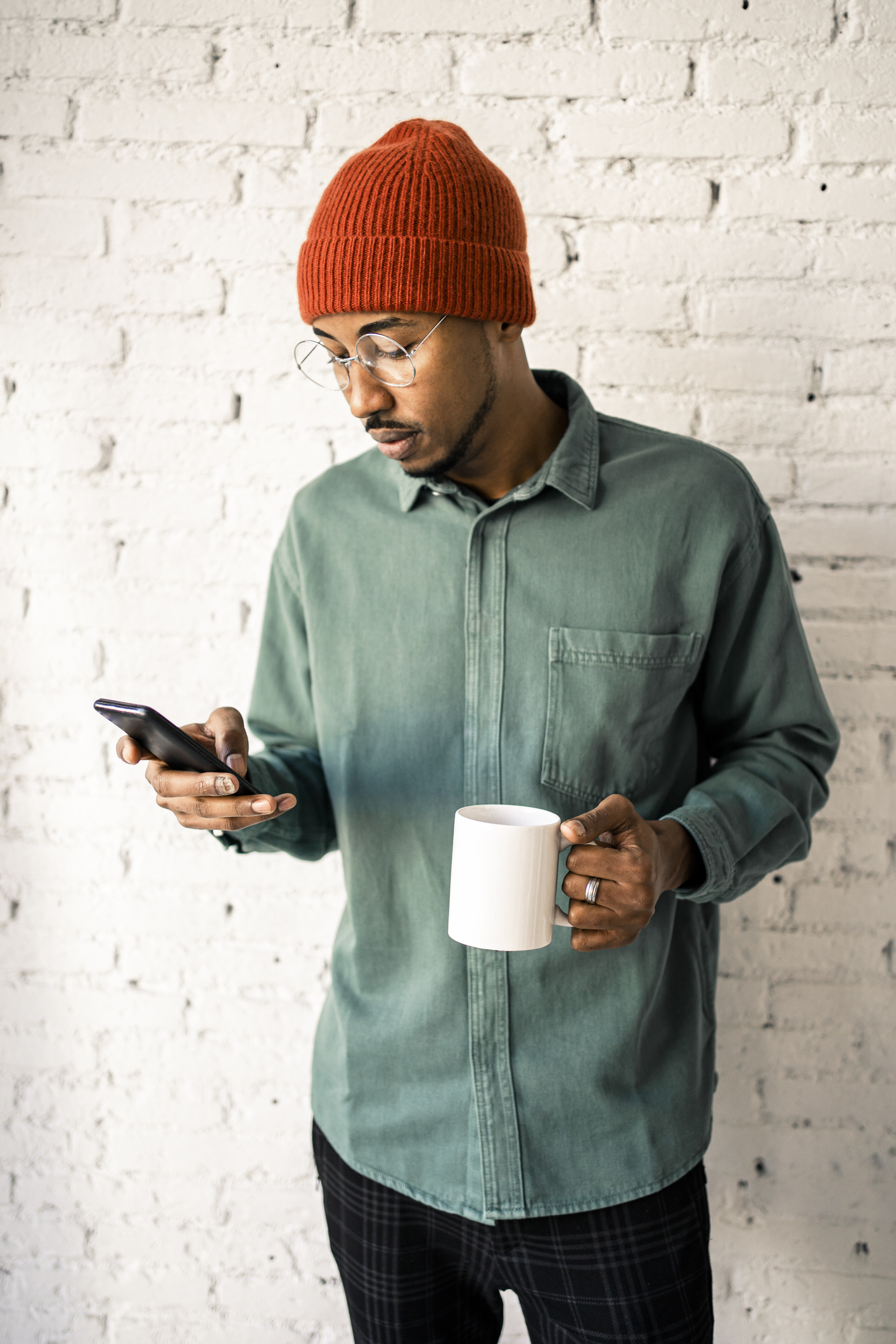 Mid adult man having coffee while using mobile phone against white brick wall