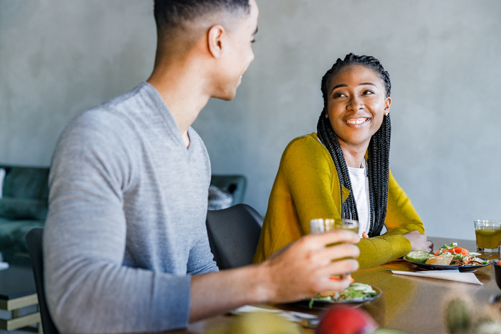 Happy black couple talking during meal at dining table.