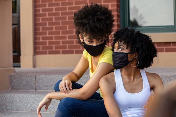 Women wearing masks and sitting back to back