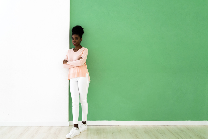 Young woman standing with arms crossed against multi colored wall
