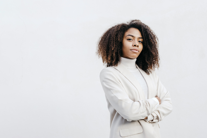 Confident young woman with arms crossed standing against white wall