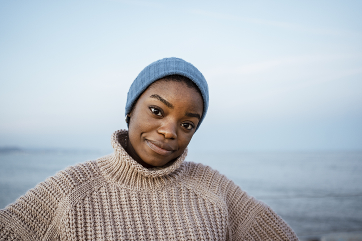 Young woman with knit hat staring while standing against sky