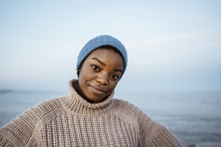 Young woman with knit hat staring while standing against sky