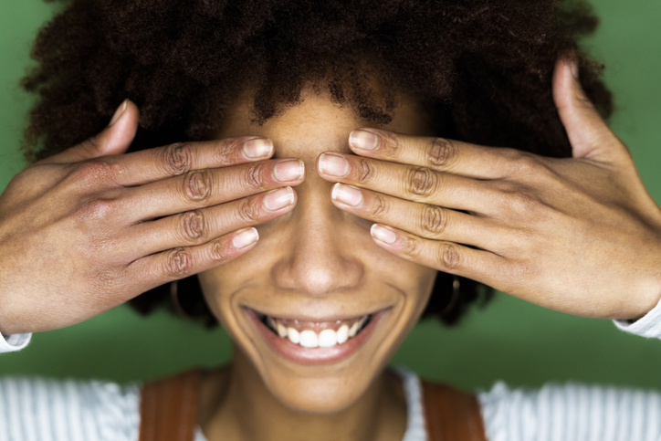 Happy young woman covering eyes with hand against green wall in new home
