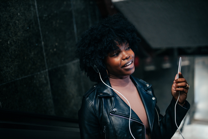 Afro woman with earphones using her cellphone while on escalator