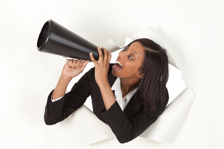 Businesswoman emerging through hole in paper shouting into a bullhorn