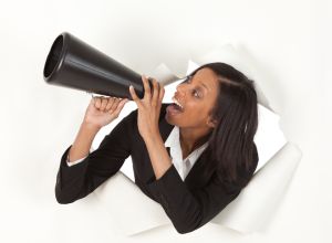 Businesswoman emerging through hole in paper shouting into a bullhorn