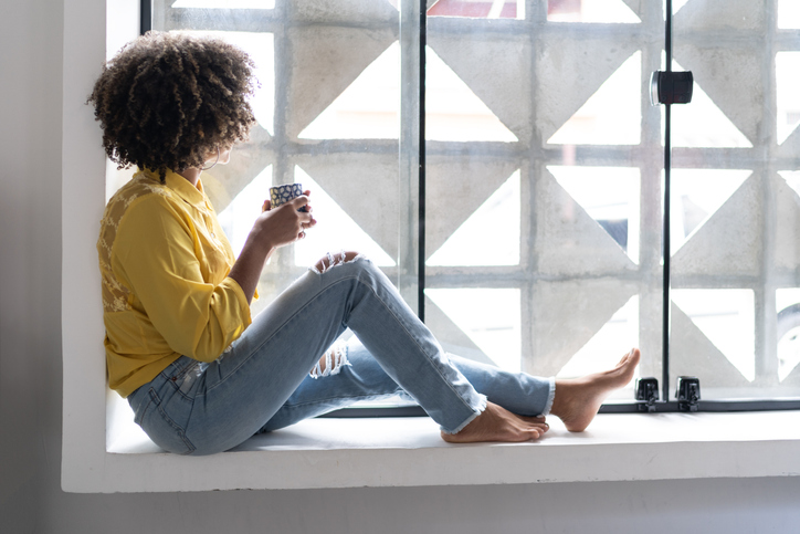 Young woman drinking coffee relaxing on window sill at home