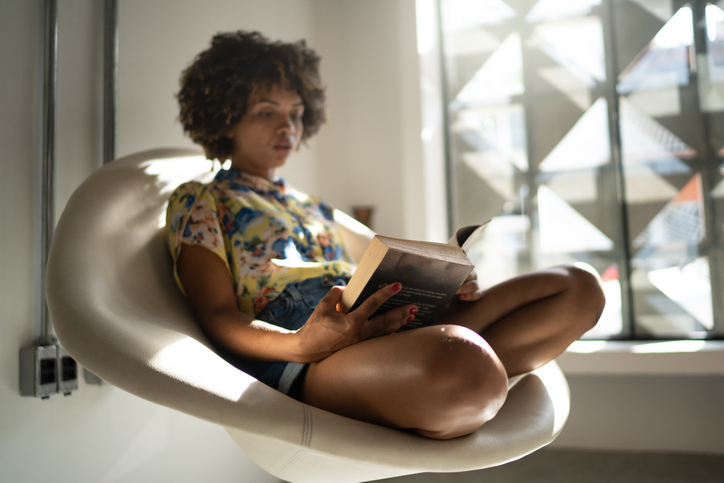 Young woman sitting on a chair reading a book at home