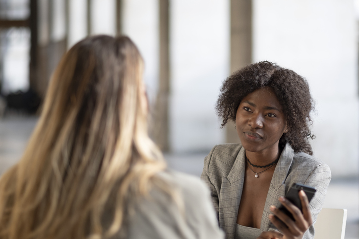 Two young female business women - one African, another Caucasian meeting outdoors