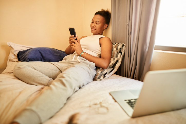 Smiling young woman using a cellphone on her bed