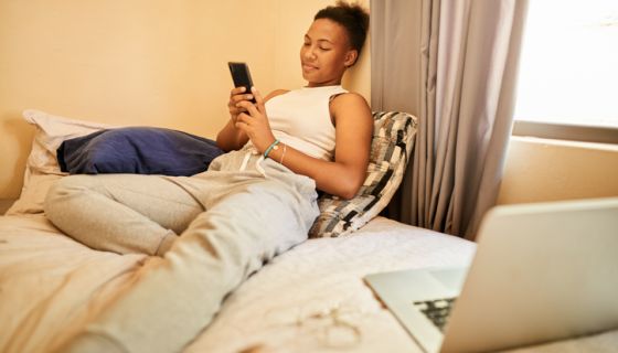 Smiling young woman using a cellphone on her bed