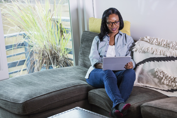 Mature black woman relaxing on sofa using digital tablet