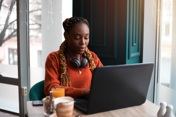 Close-up portrait of young african woman using laptop in cafe.
