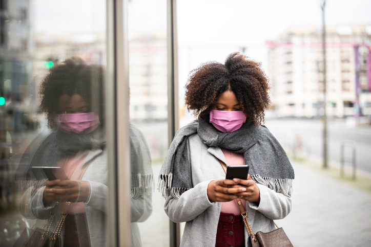 African female with face mask walking in city using phone