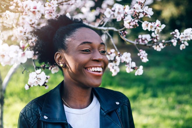 Beautiful young black girl smiling against blossom spring trees.