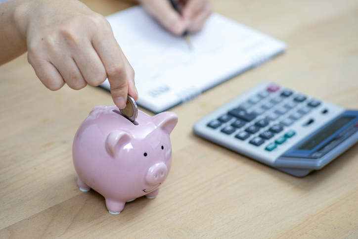 Woman hand throwing coins into piggy bank.