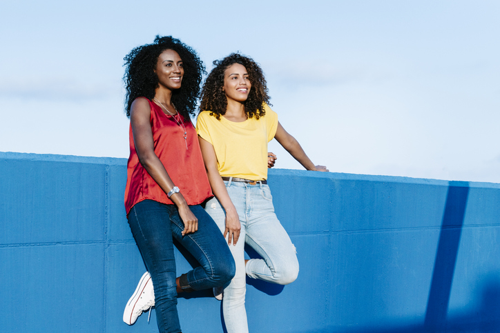 Lesbian couple looking away while standing at blue retaining wall against sky