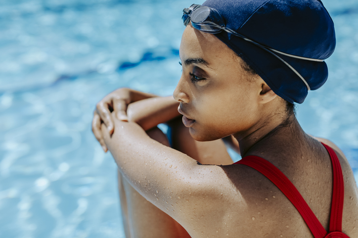 Young woman with swimming cap and goggles relaxing at poolside after swimming