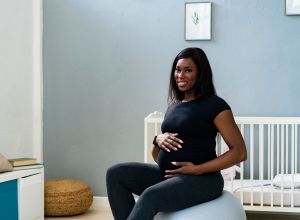 Happy pregnant young woman sitting on fitness ball at home