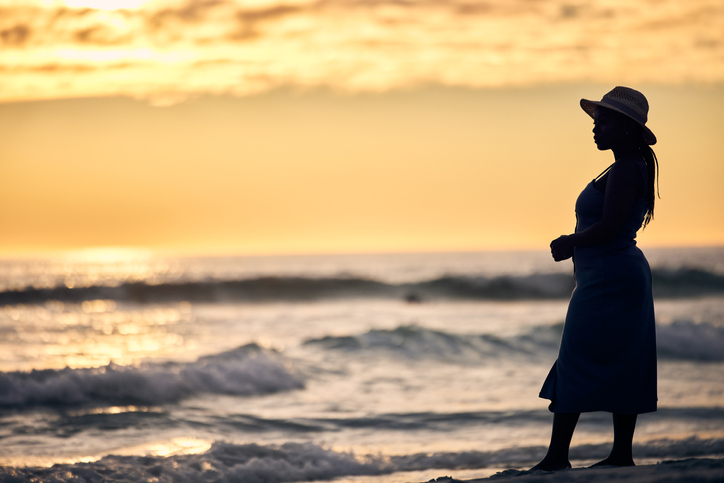 Shot of an unrecognizable woman walking along the beach at sunset