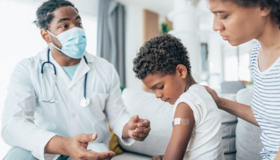 A young Black boy receives a shot from a Black doctor.