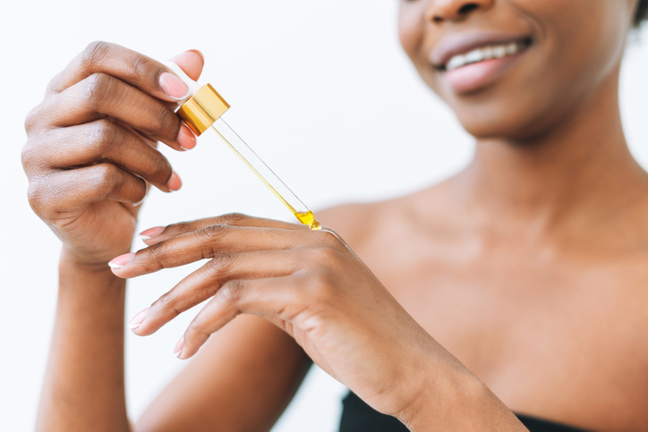 Beauty Portrait Of Smiling African Young Woman In Underwear With Cosmetic Oil For Hands And Body