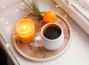 Cozy winter home interior details, cup of coffee, wooden tray, tangerine and candle. Window sill. Still life for Christmas.