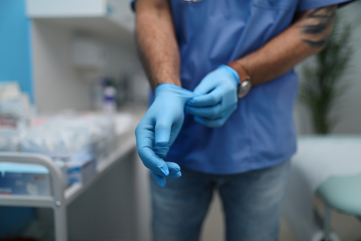 Unrecognizable male doctor putting on surgical gloves indoors in hospital.