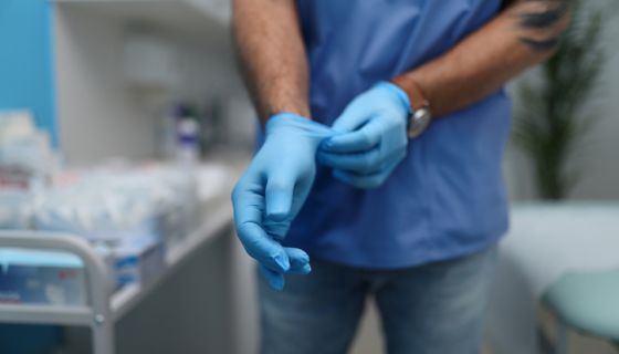 Unrecognizable male doctor putting on surgical gloves indoors in hospital.