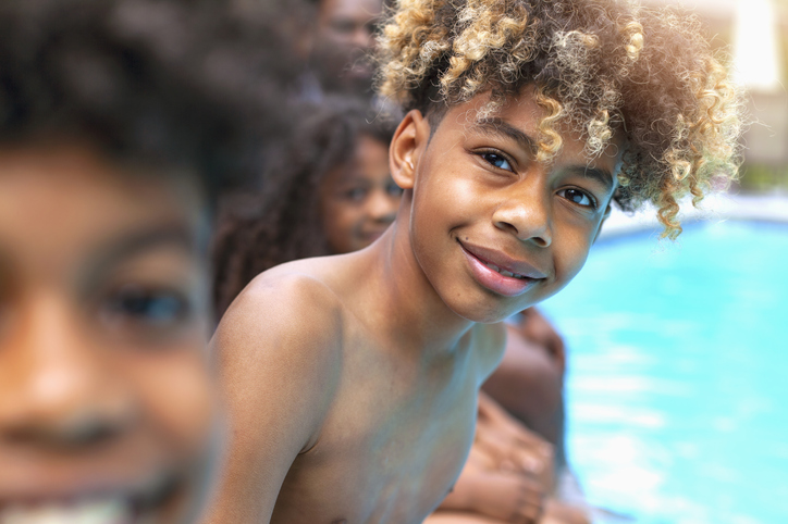 Portrait of African-American boy sitting by swimming pool with siblings