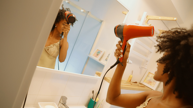 Black woman blow drying her hair in a bathroom