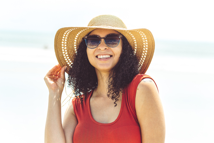 Portrait of happy carefree Afro-Caribbean woman on wearing straw sunhat on vacation in tropical paradise