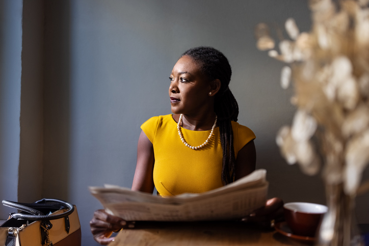 Woman with newspaper sitting at cafe looking away